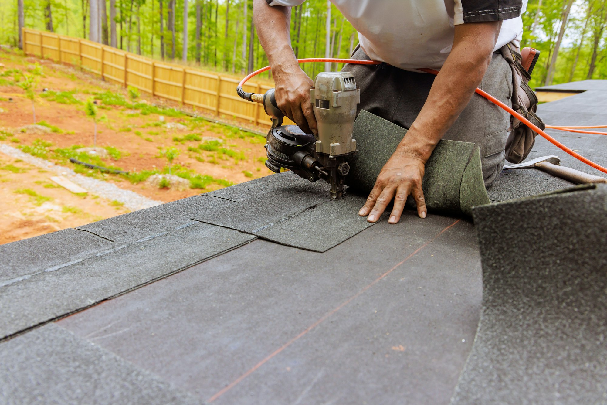 Installation of new asphalt bitumen shingles using an air pneumatic nail gun by a roofer